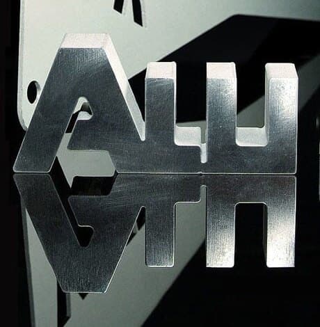 Dicke Werkstücke aus Metall: ausgeschnittene Buchstaben, die sich auf schwarzem Grund spiegeln